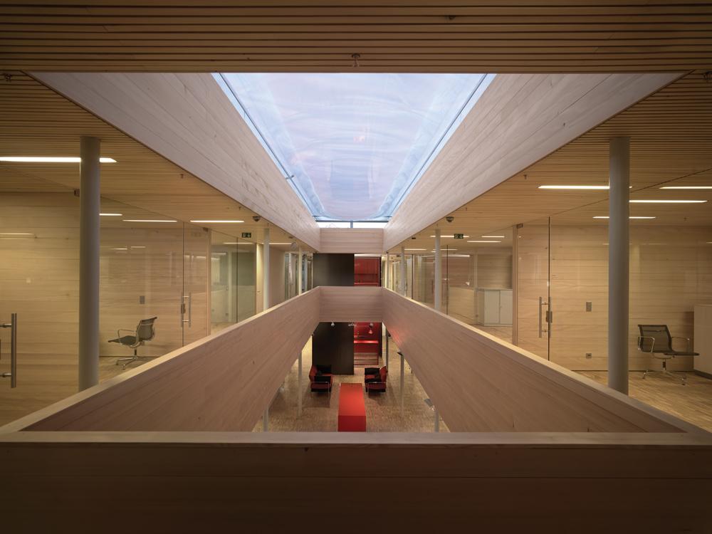 Ein transparentes Pneudach überspannt das zweigeschossige Atrium. Auch die umliegenden Büros profitieren durch raumhohe Verglasungen zum Atrium hin  von dem zusätzlichen Tageslichteintrag von oben.