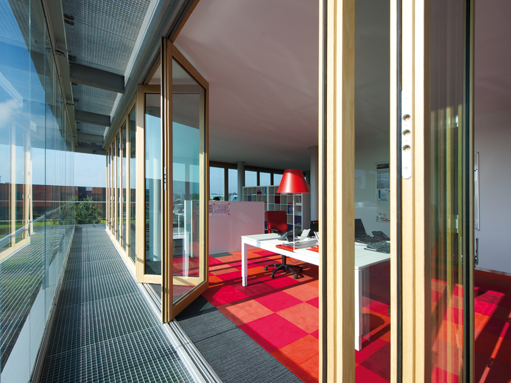 Die Co₂mfort-Doppelfassade basiert auf der Idee des Doppelfensters. Den Raumabschluss bildet die wärmegedämmte Glas-Faltwand SL 65 aus Holz. Davor befindet sich das transparente Schiebe-Dreh-System SL 25 XXL als ungedämmte Glasebene. Durch die doppelte Fassade entsteht ein begehbarer Fassadenkorridor, der das Gebäude umhüllt. Beide Fassadenebenen lassen sich vollständig auffalten, sodass sich  je nach Witterung die Innenraumtemperatur manuell regeln lässt.