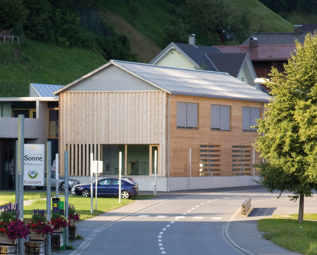 Der Massivholzbau beherbergt den Kindergarten und die Aufenthaltsräume der Feuerwehr. Die Fahrzeughalle, Werkstätten und Sanitärräume liegen zurückversetzt in dem Baukörper aus Beton.