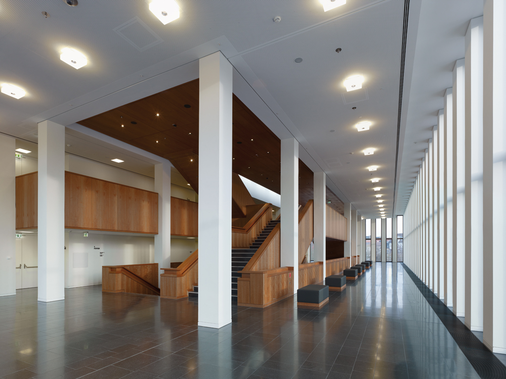 Eine großzügige Treppenanlage setzt im Foyer architektonische Akzente. Die Bekleidung aus amerikanischem Kirschholzfurnier kontrastiert mit den weißen Stützen, Wand- und Deckenflächen.