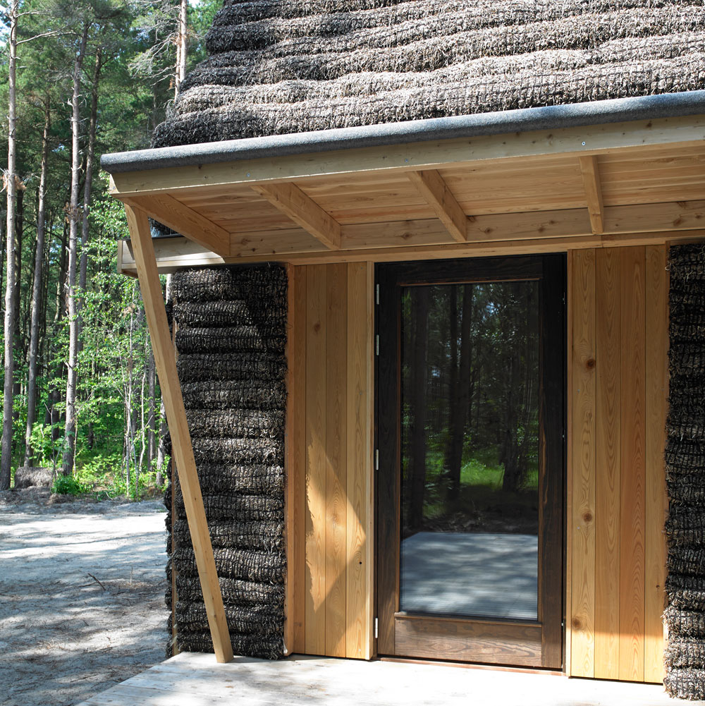 Gebäudeecke im Südwesten. Die Fassadenbekleidung, die Unterseite des Vordachs sowie der Terrassenbelag bestehen aus Lärchenholz.