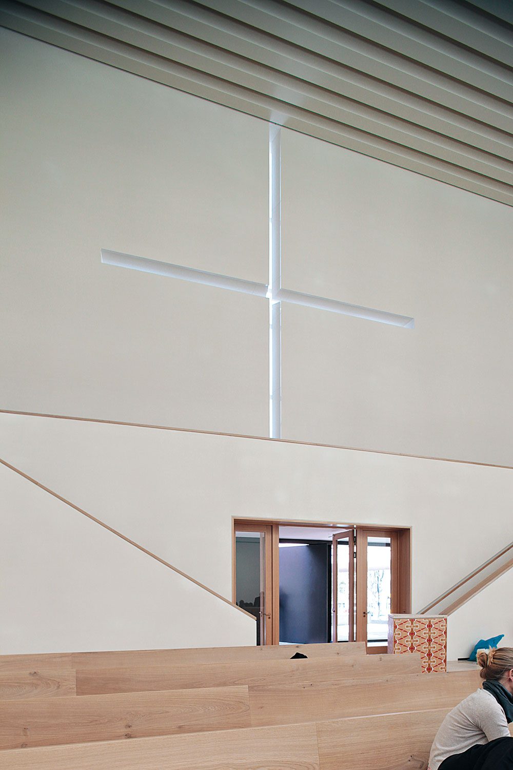 Das Fensterkreuz in der Westfassade des Kirchenraums über dem Eingangsportal ist in das Höhenraster der Natursteinfassade integriert.
