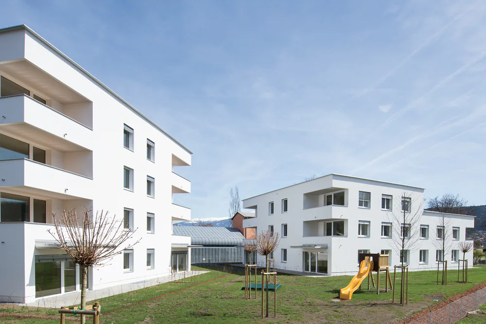 Wohnanlage in Innsbruck, Architekten VoglFernheim 2015. Der viergeschossige Neubau links im Bild wurde im Sommer 2015 als erster Geschosswohnbauten als Passivhaus Plus zertifiziert. Sein Energiekonzept umfasst eine Grundwasserwärmepumpe sowie Solarthermie und eine Photovoltaikanlage.