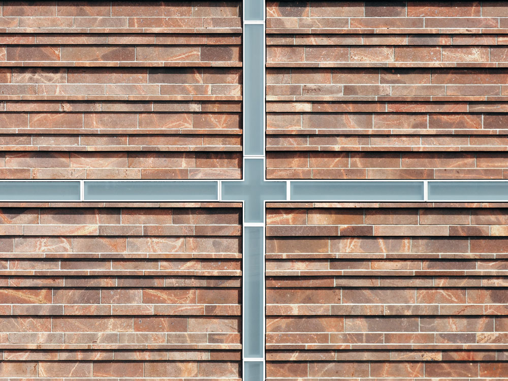 Das Fensterkreuz in der Westfassade des Kirchenraums über dem Eingangsportal ist in das Höhenraster der Natursteinfassade integriert.