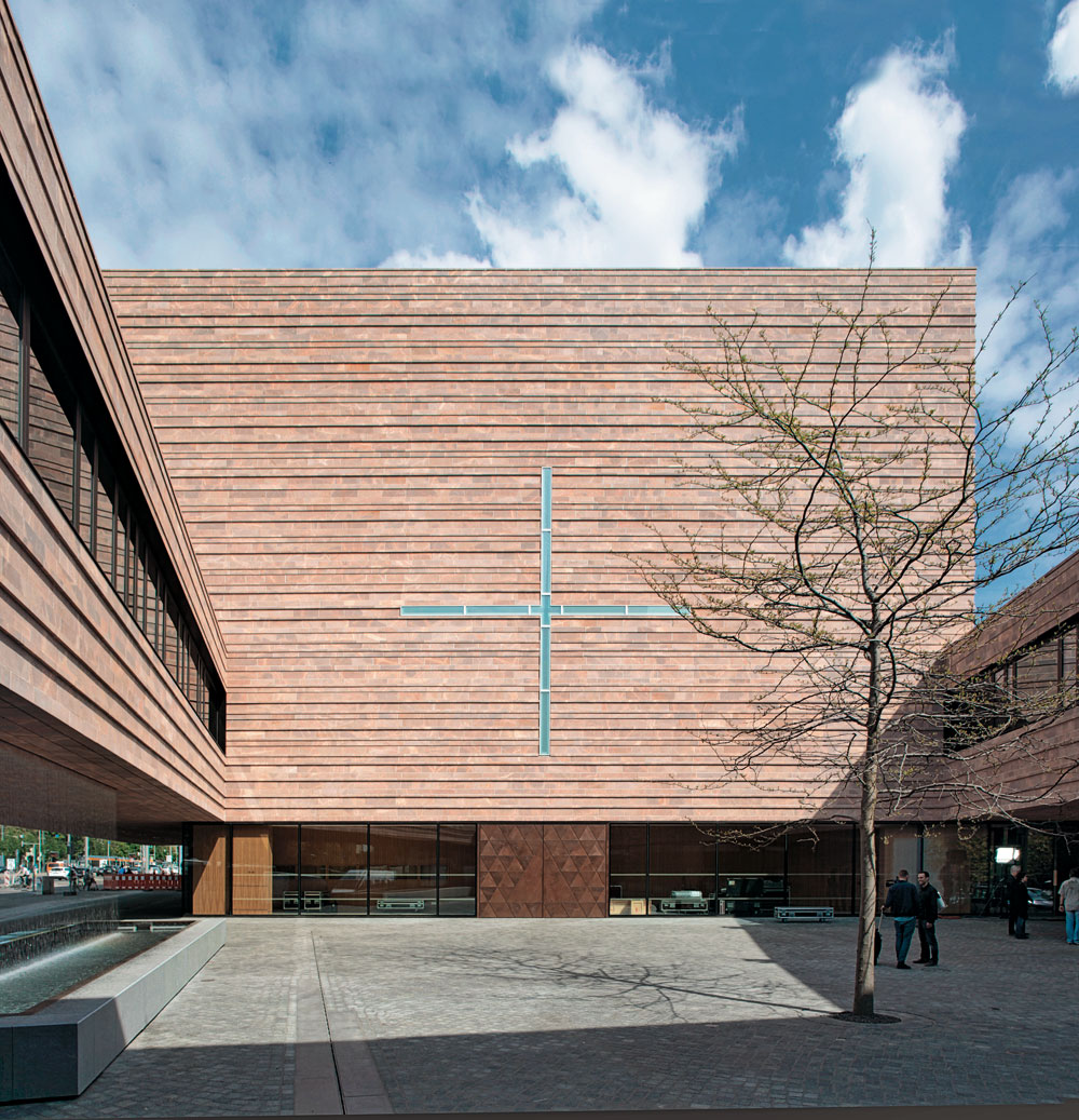 Das Fensterkreuz in der Westfassade des Kirchenraums über dem Eingangsportal ist in das Höhenraster der Natursteinfassade integriert.