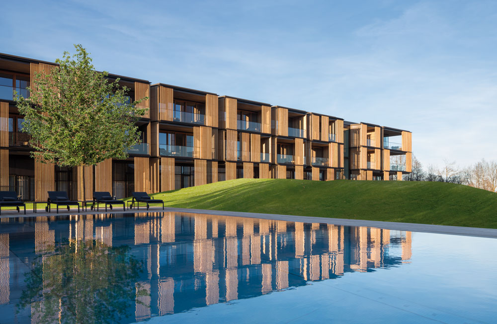 Die quadratische Anlage wurde optimal in die Landschaft der Umgebung eingebettet. Die Gemeinschaftsräume und der medizinische Bereich orientiert sich zu einem begrünten Atrium, während die Zimmer und Suiten den Gästen Panoramablicke auf den See und die Berge offerieren.