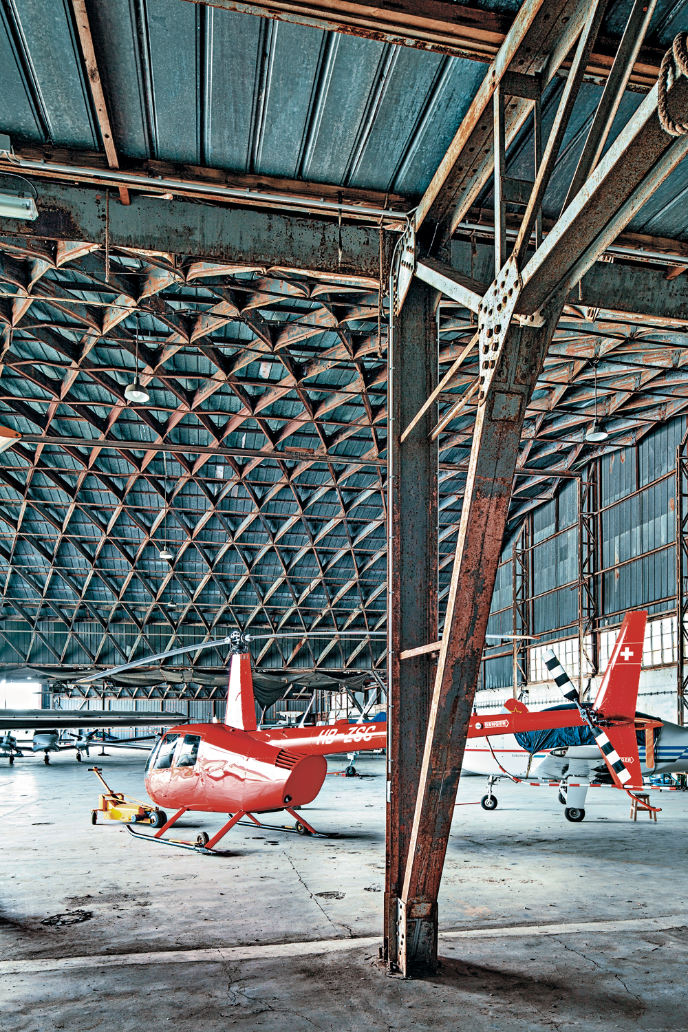 Hangar auf dem ehemaligen Militärflughafen Oberschleißheim bei München (Zustand 2015): Detailansicht eines Tragwerksknotens, Axonometrie einer Tonnenhalle mit Verbindungsrahmen zur Anschlusstonne, Blick in die Halle mit seitlicher Rahmenkonstruktion (im Vordergrund)