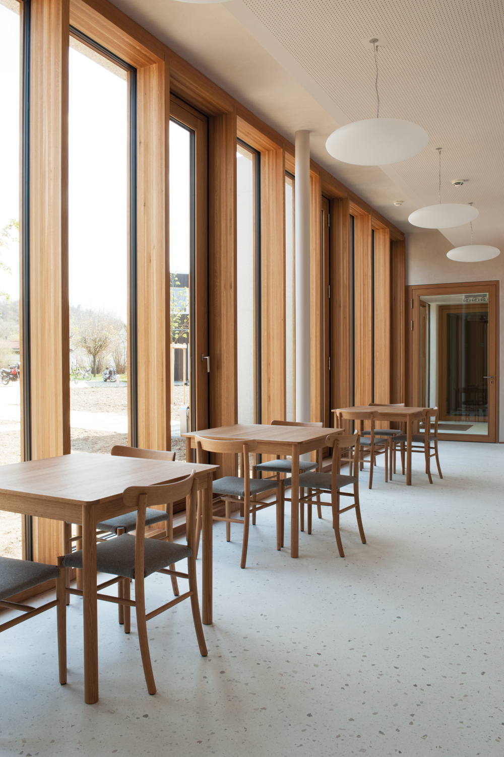 In der Innenraumgestaltung setzt sich der präzise Entwurfsansatz fort. Alles ist harmonisch aufeinander abgestimmt. Die Möblierung der Caféteria nimmt z. B. den Holzton der Fenster wieder auf.