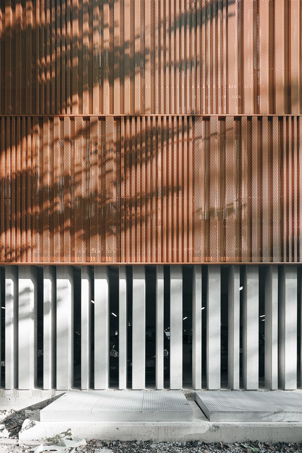 Die Fassade des neuen Parkhauses der Inselhalle in Lindau von Auer Weber besteht aus rechtwinklig gekanteten, kupferfarben pulverbeschichteten Aluminium-Lochblechen, die – ähnlich einem textilen Vorhang – je nach Standpunkt des Betrachters entweder luftig leicht oder blickundurchlässig wirken.