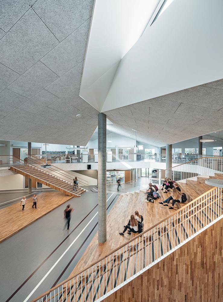 Das Herzstück des Schulhauses ist die zentrale Halle, deren nach Norden und Süden ausgerichtete
Oberlichter warmes und kaltes Licht in den Raum fallen lassen. Zu regulärer Unterrichtszeit nutzen die Schüler die Sitzstufen zum Lernen oder für Teamarbeit. Auf der Galerie im Obergeschoss ist
die Bibliothek untergebracht, die jeder zu jeder Zeit nutzen kann.