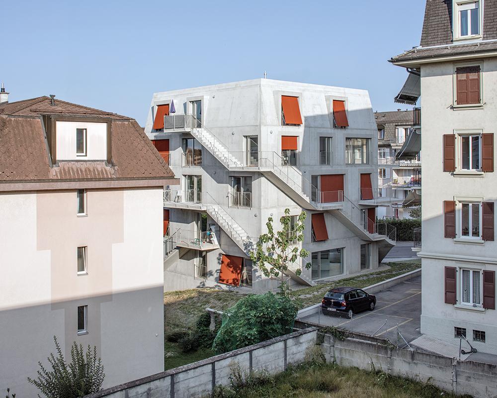 Die roten Fallarmmarkisen prägen die Fassade des Wohnhauses. Die Sichtbetonfassaden sind innen gedämmt und mit Gipskarton verkleidet.