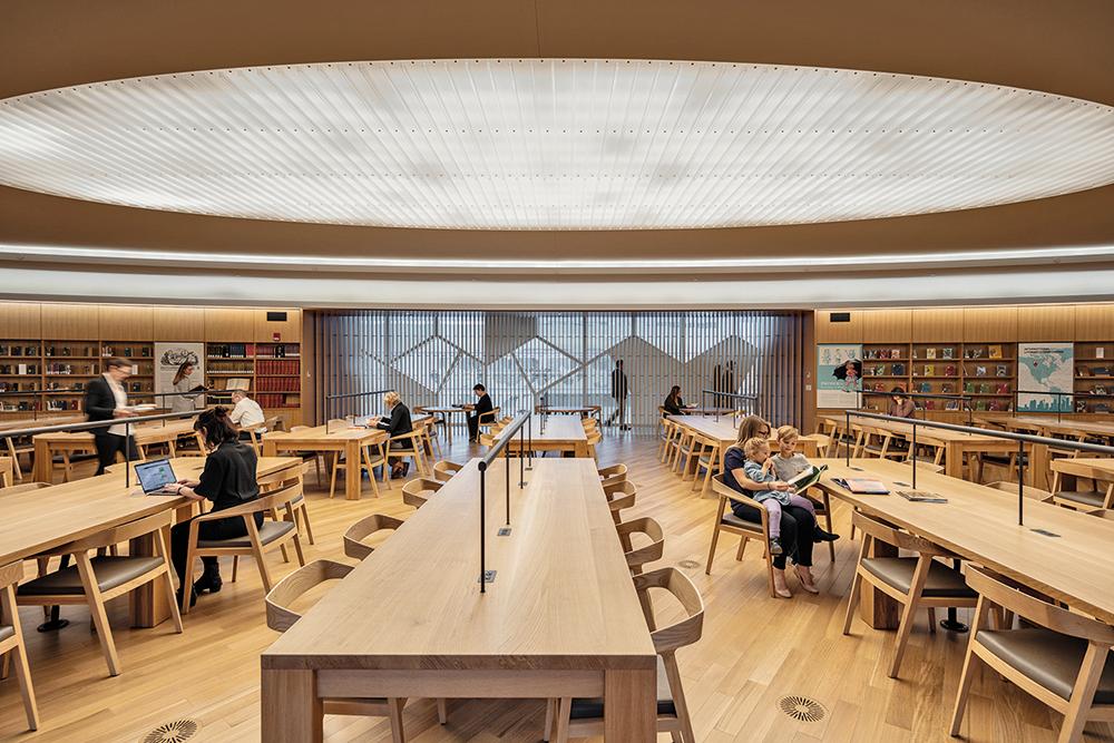 Der große Lesesaal ist nur durch ein filigranes Gitter aus Holzlamellen vom Atrium getrennt. Eine ovale Lichtdecke betont die konzentrierte Atmosphäre im Raum.