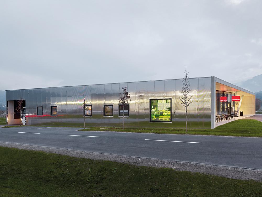Mit großen, edelstahlbeschichteten Sandwichpaneelen verlieh das Architekturbüro LAAC dem Supermarkt in Weer eine edle Anmutung. Nur die Eingangsfront öffnet sich voll verglast zum Parkplatz.