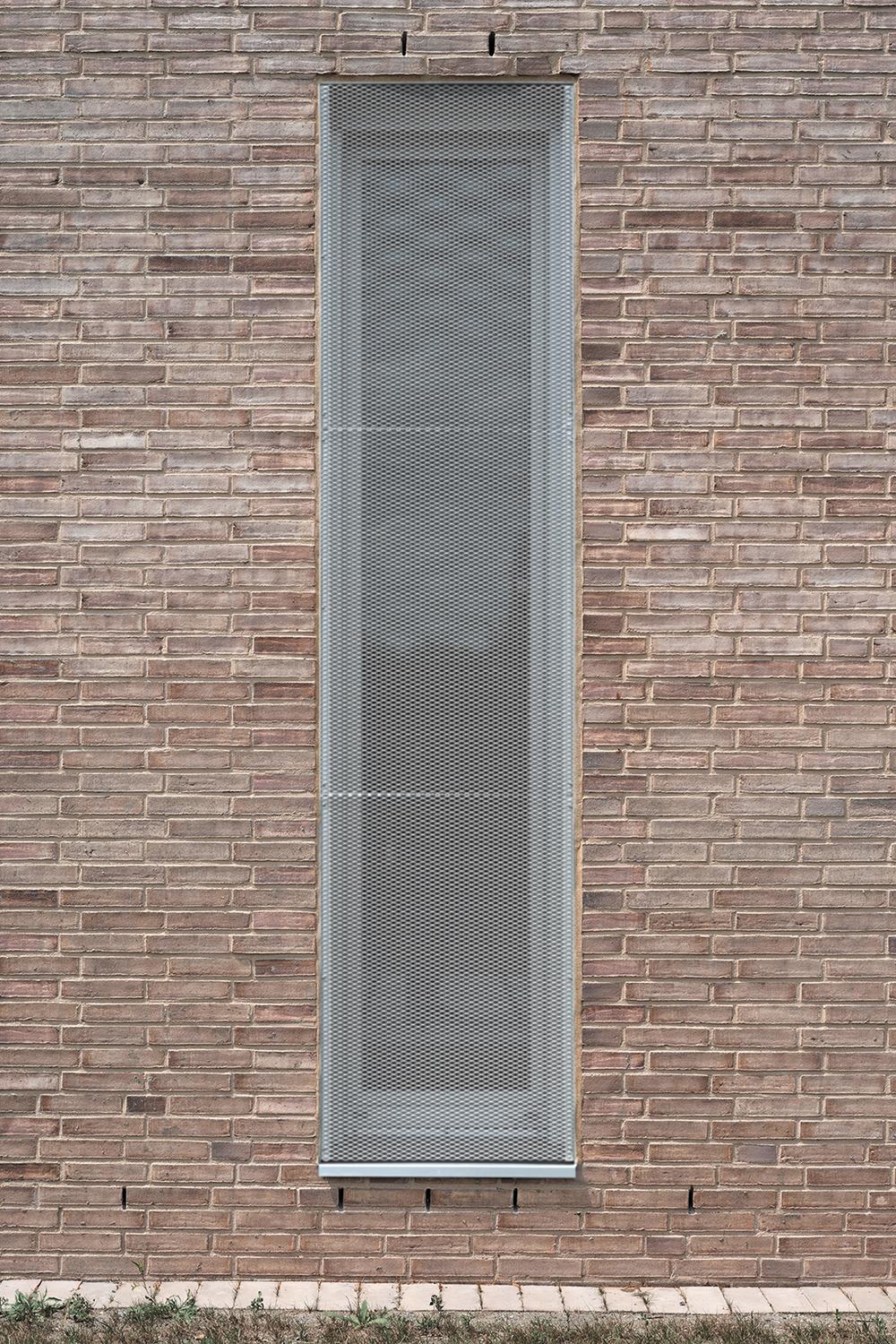 Die hohen, schmalen Entrauchungsöffnungen aus Metall erinnern an Fenster. Sie brechen den Maßstab des Gebäudes und zonieren die Fassade.