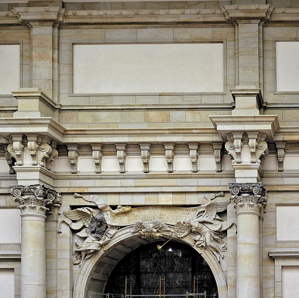 Die wenigen erhaltenen Originalsteine, die Kriegszerstörung und Abtransport überstanden haben, sind als Fragmente in die rekonstruierte Fassade integriert und heben sich durch die dunkle Steinfarbe ab.