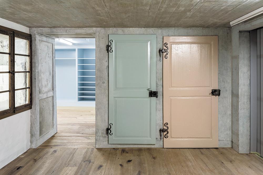 Im Eingangsbereich zu den Werkstätten erinnert ein Fenster daran, wo das Haus früher endete. Heute schafft es den Sichtbezug zur Galerie Oblique im Erdgeschoss. Hinter den pastellfarbenen Türen ist die Garderobe untergebracht.