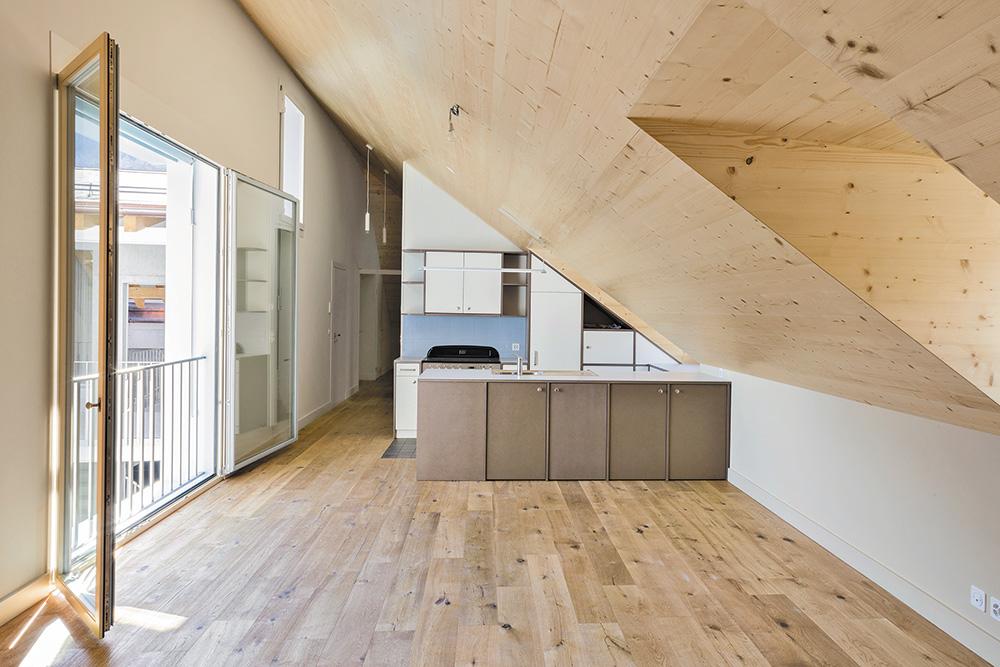In der Dachgeschosswohnung prägen naturbelassene Holzoberflächen den Raum. Die dezent ornamentale Holzverkleidung des Innenhofs ist hingegen in Erinnerung an die historischen Gebäude blau gestrichen.