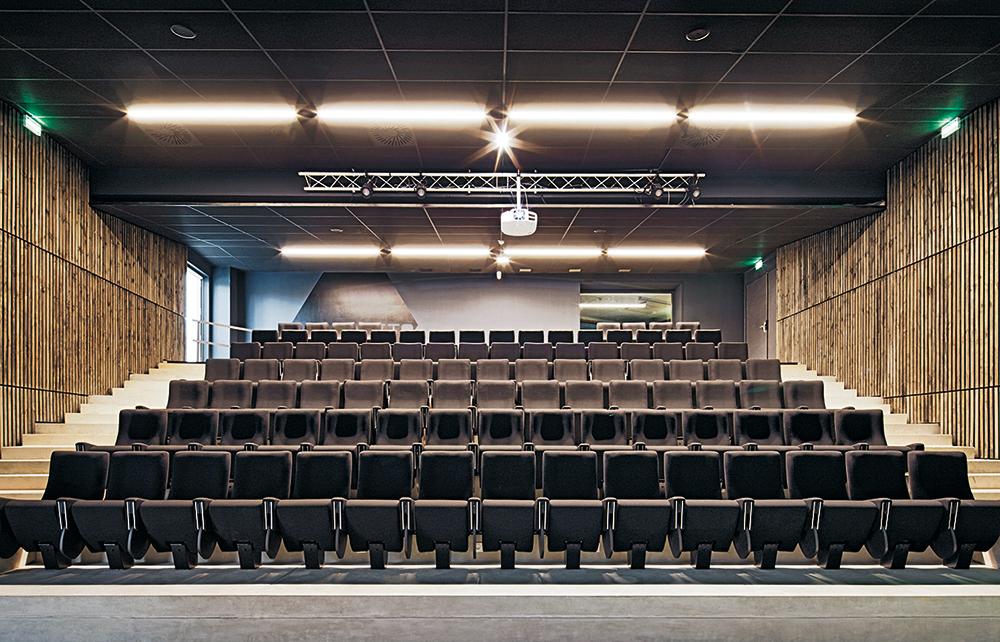 Der neue Hörsaal ist von außen unsichtbar in den Hang eingegraben. Die Wandbekleidung aus vertikalen Holzlatten zieht sich von den Türlaibungen bis ins Innere.