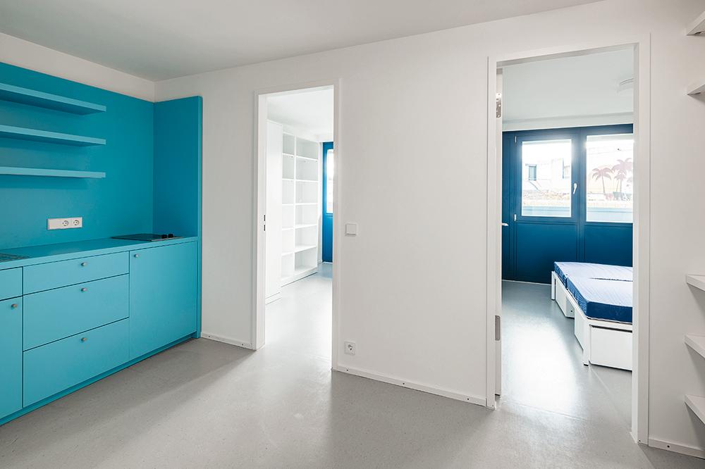 The built-in furniture in fresh Olympic blue is part of the inventory in all the dwellings, as are white beds and tables.