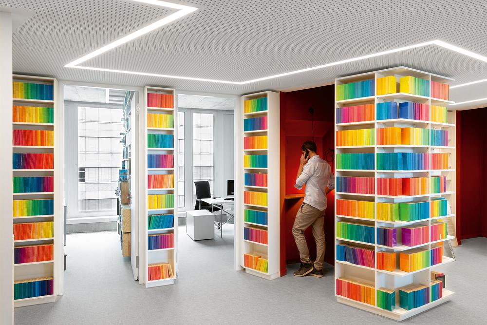 Farbige Buchrücken und kräftige Farbakzente auf den Möbeln kontrastieren mit dem neutral gestalteten Innenausbau.