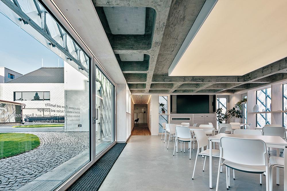 Durch die Glasschiebetüren der Cafeteria im Erdgeschoss fällt der Blick auf den zweiten, mit schwarzen Faserzementplatten bekleideten Neubau.