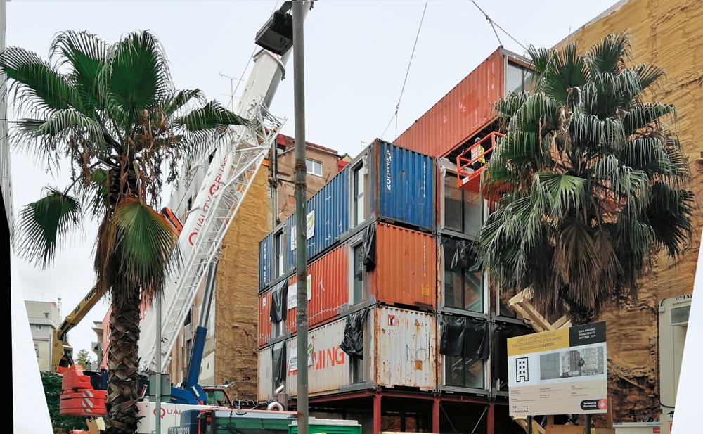 Ein Autokran liefert die ausgebauten Schiffscontainer an und stapelt sie auf die Tragstruktur, die das Erdgeschoss bildet.