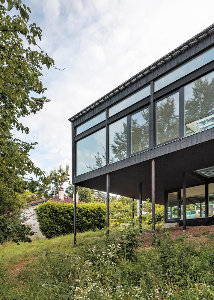 Die raumhohen Fenster auf der Ostseite und die kreisrunde Aussparung an einer der beiden Terrassen sind die einzigen Öffnungen in der schwarzen Holzfassade.