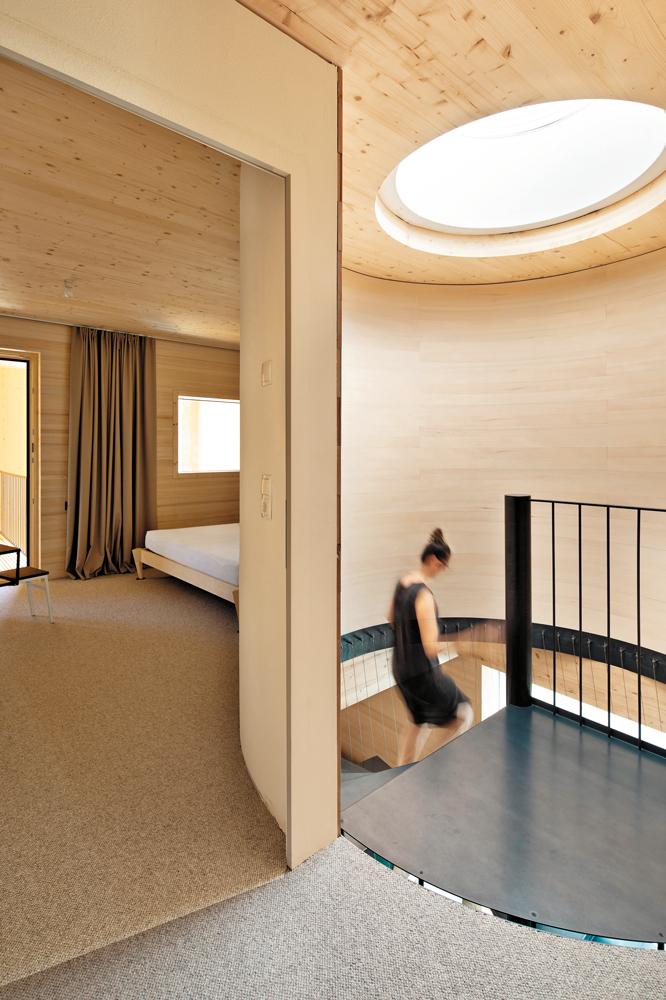 Das oberste Geschoss mit den Schlafzimmern ist kleinteiliger gegliedert als die unteren und hat eine Flachdecke aus Brettsperrholz. Eine Lichtkuppel bringt zusätzliches Tageslicht ins Haus.