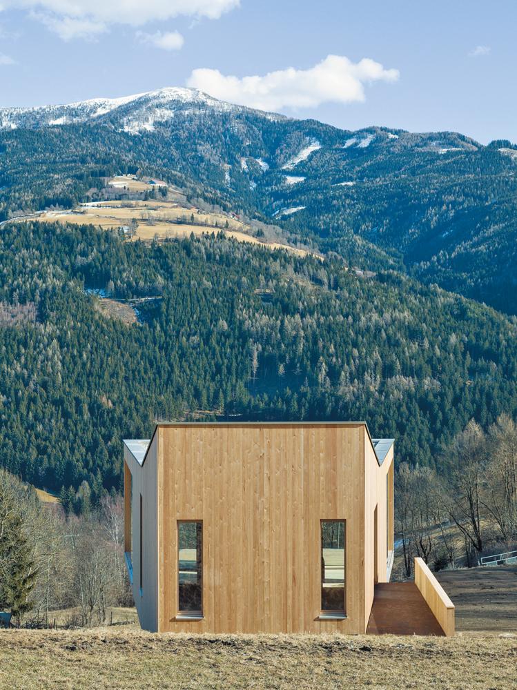 Der trapezförmige Grundriss des Hauses öffnet sich zum Bergpanorama auf der gegenüberliegenden Talseite. Die hochgezogene Rückwand dient als Windschutz für die kleine Dachterrasse.