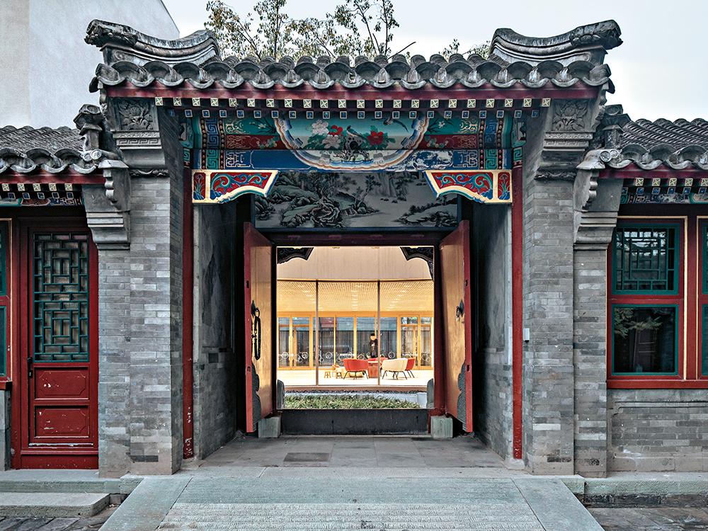 The grand 18th century entrance gate is covered in grey tiles like the rest of the historic courtyard house, which frames the view into the rooms of the new kindergarten.