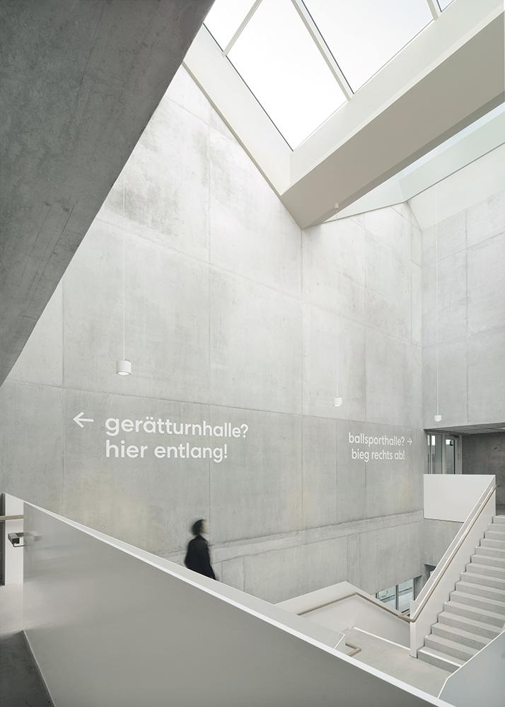 In den Innenräumen setzt sich das Weiß der Fassade an Prallwänden, Streckmetalldecken und Brüstungen fort – elegant kombiniert mit hellgrauem Sichtbeton.