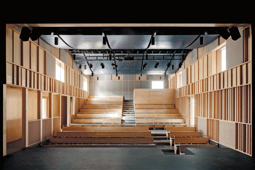 Die kleinteilige Fassadengliederung kehrt auch im Inneren des Theatersaals in abgewandelter Form wieder. Dort dämpfen graue Akustikpaneele den Schall.