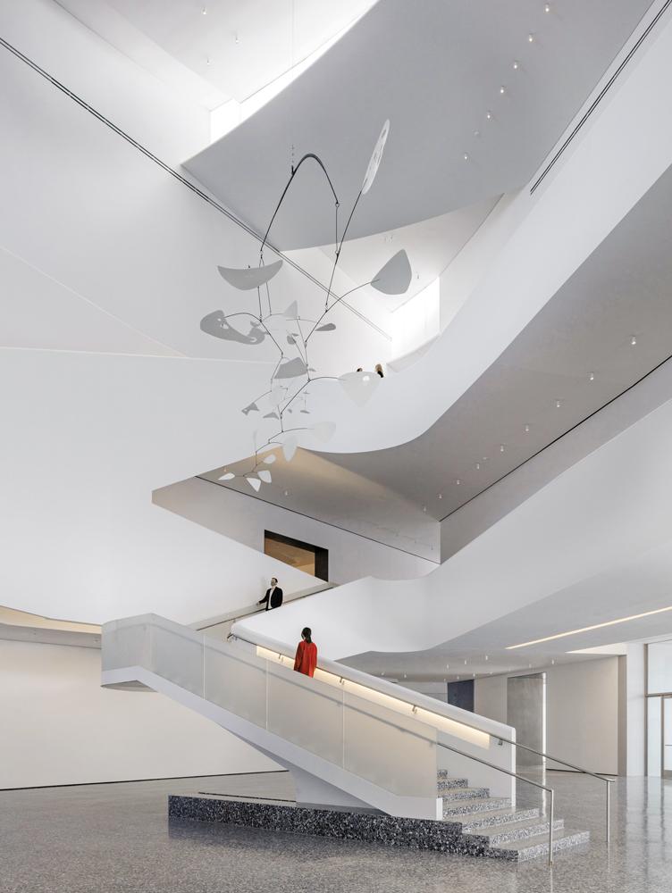 Die verglasten Seitenwände der Dachsegmente fluten die Eingangshalle mit Tageslicht. Eine ausladende Treppe führt die Besucher und Besucherinnen zu den Galerien, die sich um ein Atrium gruppieren.