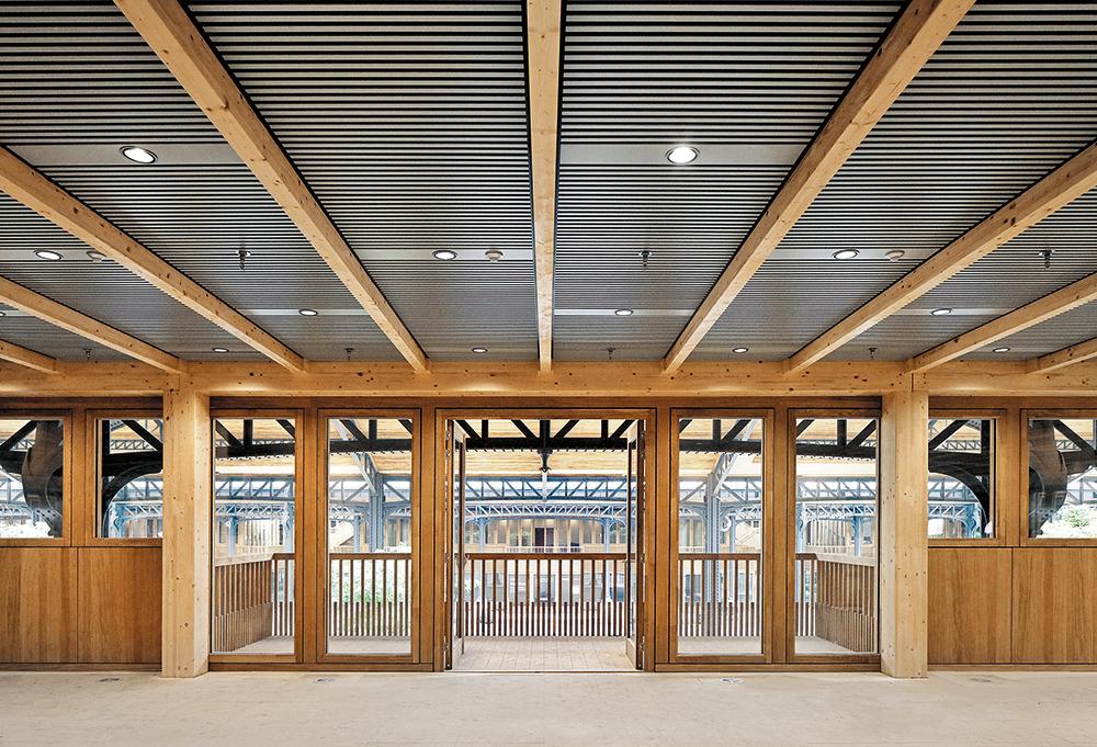 Im Innern der Pavillons kehrt die geriffelte Fassadenstruktur an den angehängten Holz- und Kühldecken wieder. Darin sind auch Leuchten, Brandmelder und Sprinkler integriert.