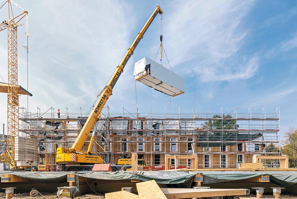 Das Gebäude aus vorgefertigten Modulen lagert auf Holzpfählen, dazwischen verläuft eine Techniktrasse.
