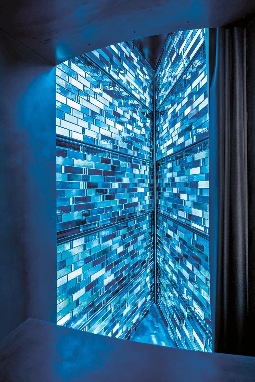 Die blaue Bleiverglasung hinter der äußeren Isolierglashülle taucht den Erkerraum tagsüber in blaues Licht. Nachts strahlt sie, elektrisch hinterleuchtet, in den Straßenraum hinaus.