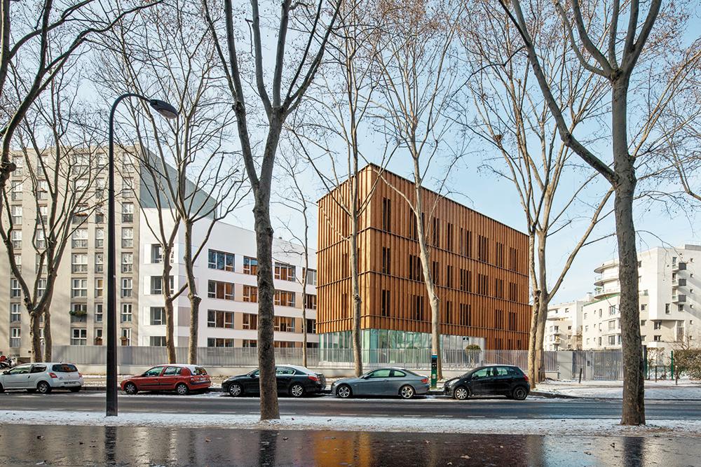 Seine Lärchenholzschalung gibt den Kopfbau als Solitär zu erkennen. Der längere, zweigeteilte Gebäudeflügel dockt an den benachbarten Wohnblock an. Beide Gebäudeteile erhielten neue, vorgefertigte Fassaden mit Strohballendämmung.