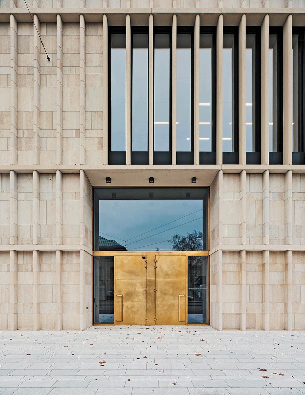 Hervorspringende Lisenen gliedern die Fassade aus gemauertem Jura-Kalkstein. Aus statischen Gründen wechselt das Material im Bereich der Fenster zu Beton.