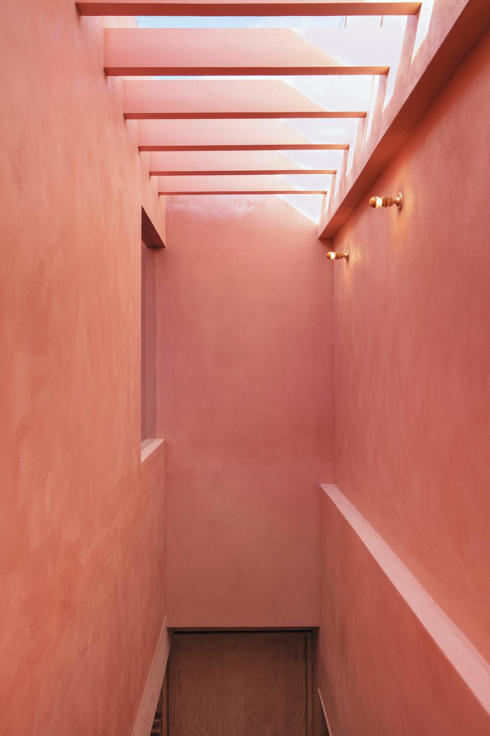 Die rot gefärbten, lehmverputzten Wände erinnern an traditionelle mexikanische Architektur. Auch der Lichtschacht über der Treppe erstrahlt in einem warmen Farbton.
