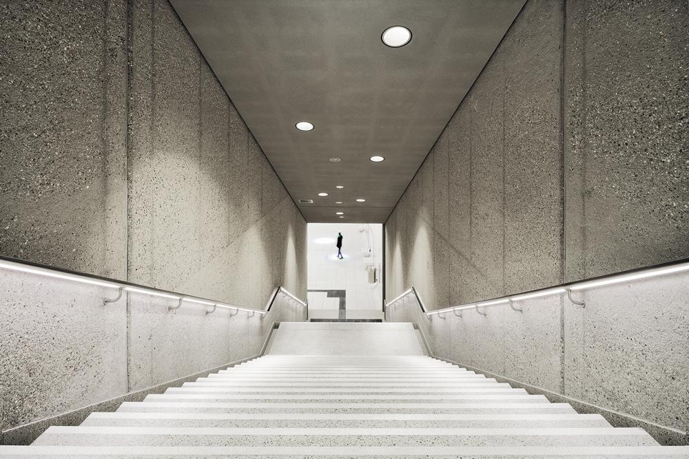Die gestockten Betonoberflächen des Zwischengeschosses sind von den Betonröhren des Rohbaus inspiriert. LED-Streifen im Handlauf lassen sie edel erscheinen.