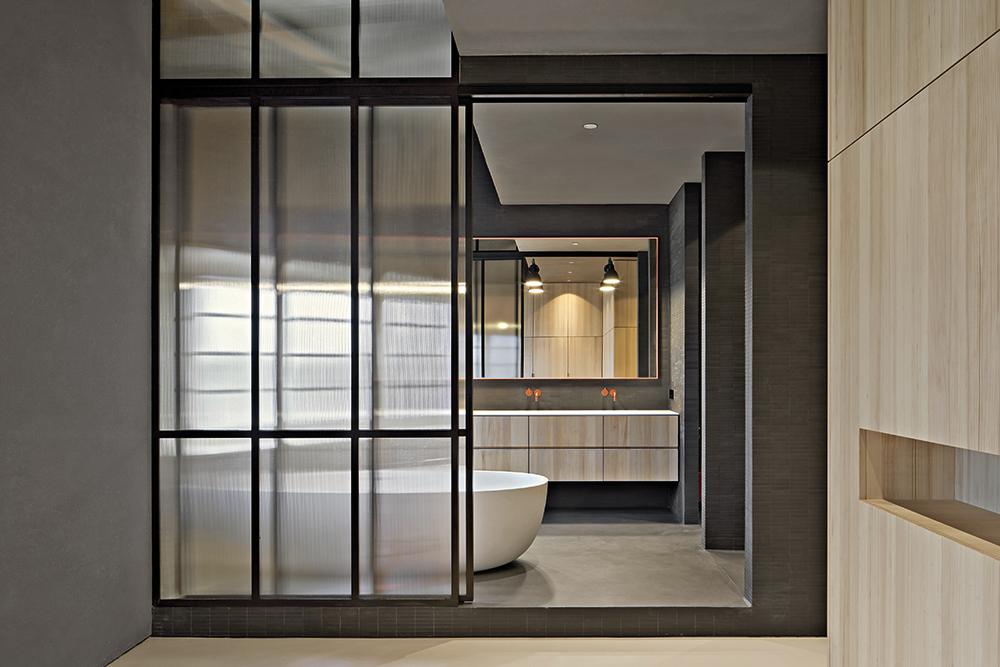 Eine schiebbare Trennwand aus Stahl und Glas schafft eine visuelle Verbindung zwischen Bade- und Schlafzimmer.