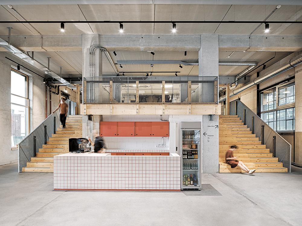 The white tile-clad countertop of the café is bordered by two broad timber staircases. They double as spaces for circulation and recreation.