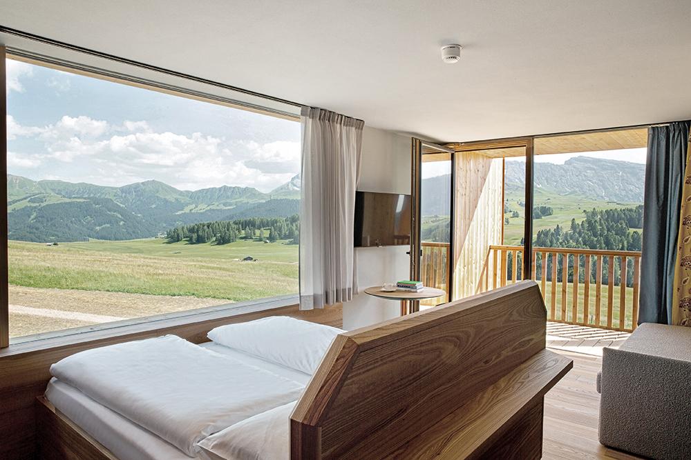 Im Zimmer Grandangolo genießen die Gäste einen Weitwinkelblick auf die Alm. Das Bett ist dazu direkt vor dem Fenster platziert.