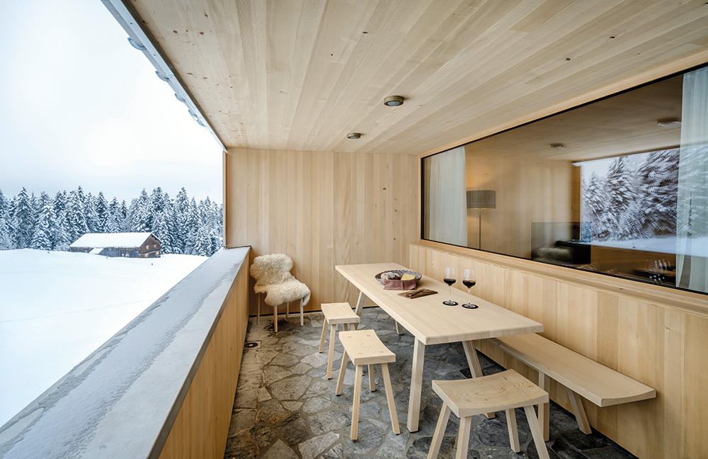 Die überdachte Veranda der kompakten Baukörper mit Holzfassade wird in der traditionellen Baukultur im Bregenzerwald „Schopf“ genannt.