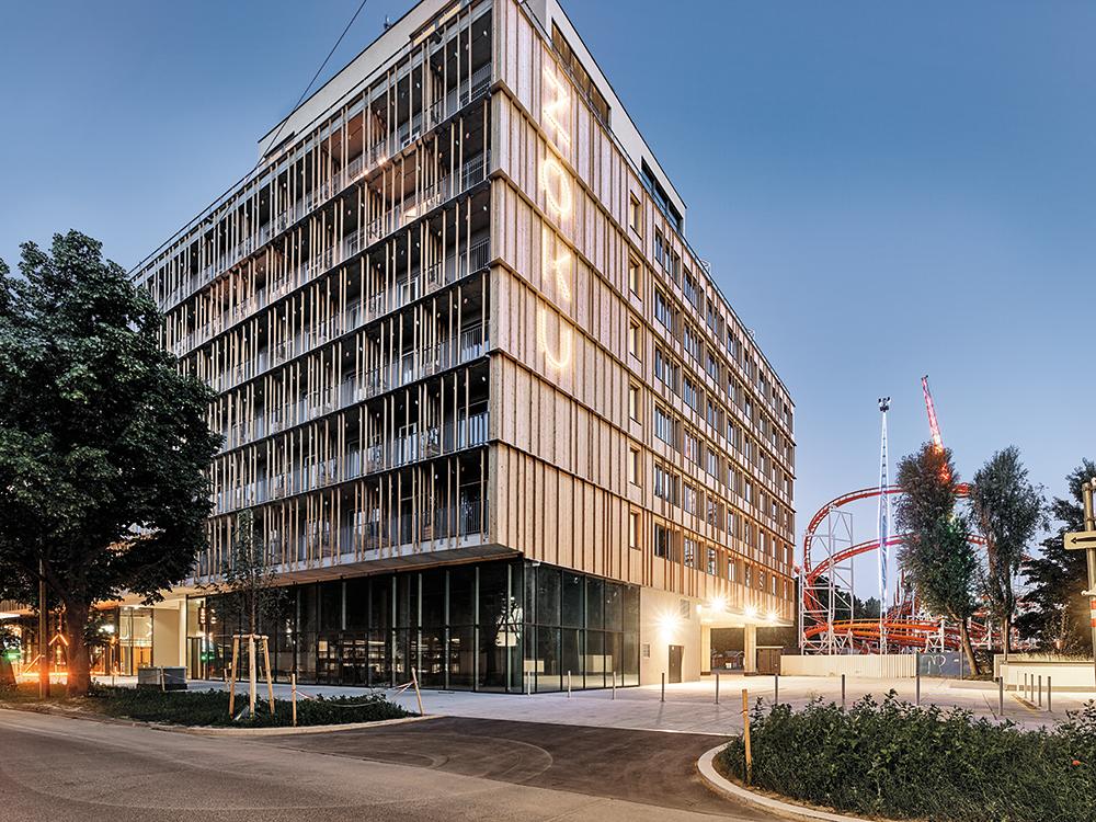 Auf der Straßenseite ist der siebengeschossige Baukörper mit Holz verkleidet. Der gläserne Sockel ist zweigeteilt. Im ­westlichen Teil befindet sich die Rezeption von Superbude, im Teil daneben der Zugang zu Zoku.