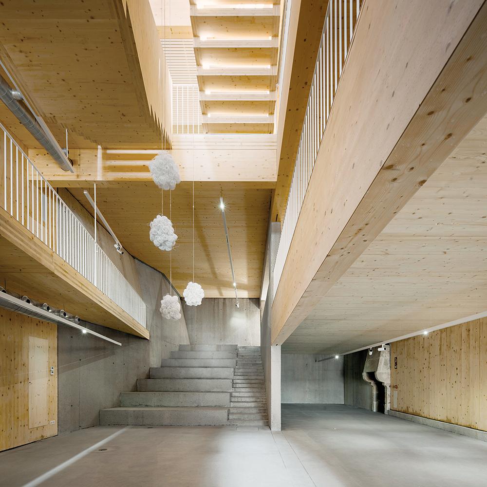 Im zweiten Obergeschoss flankieren verglaste Seminar- und Konferenzräume die offene Treppenhalle. Sitzstufen und Wände aus Sichtbeton bilden einen massiven Sockel für den Holzbau.