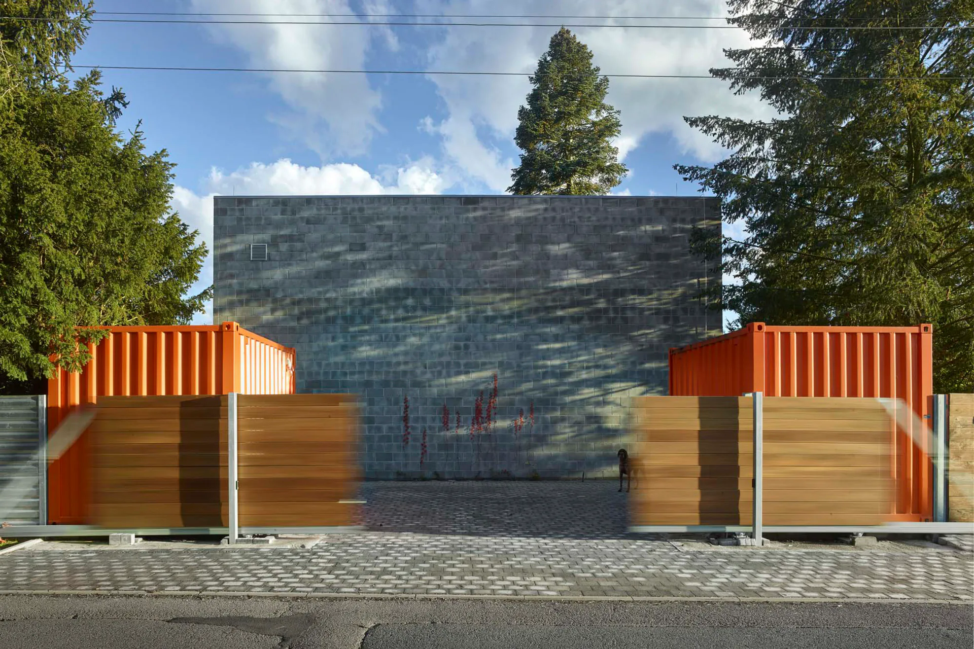 Zwei orangenfarbene Schiffscontainer rahmen die Zufahrt zum Einfamilienhaus.