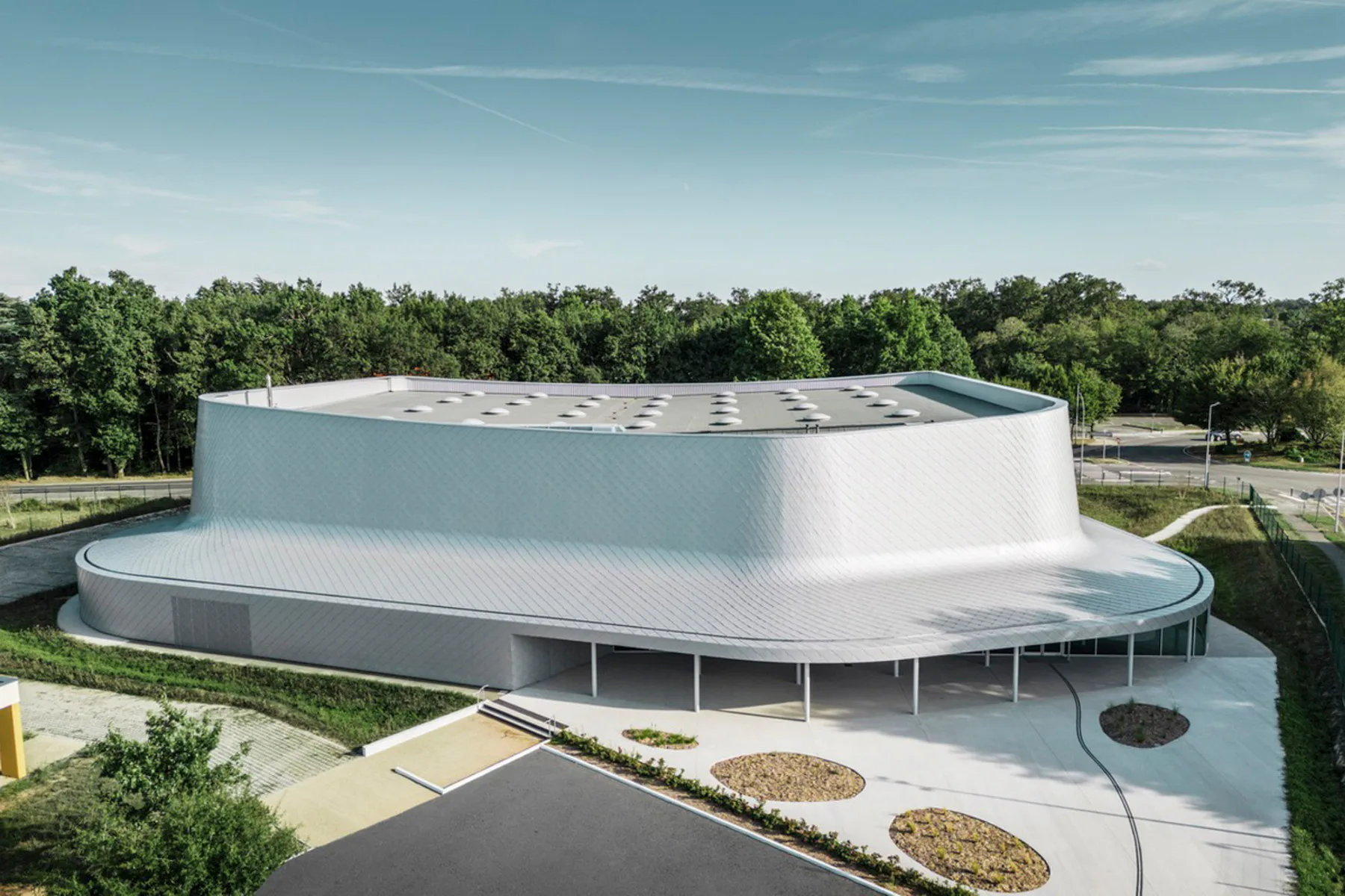 Die Sporthalle wirkt mit ihrer geschwungenen Fassade aus rautenförmigen Aluminiumschindeln wie eine metallische Skulptur.