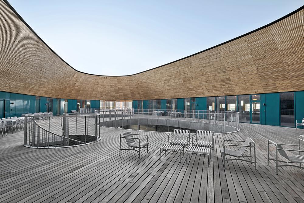 Die gemeinschaftliche Terrasse erinnert an das offene Deck eines Holzbootes. Zwei große Öffnungen verbinden beide Geschosse und die verschiedenen Aktivitäten des Gebäudes miteinander.