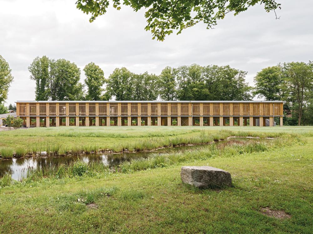 Transparent und leicht fügt sich der ­filigrane Holzbau in seine grüne Umgebung zwischen einem kleinen Teich und alten Bäumen.